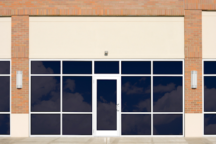 Closed storefront with dark windows and a white door under a brick facade