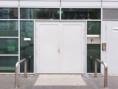 Glass-front building entrance with white double doors, metal railings, and a ramp