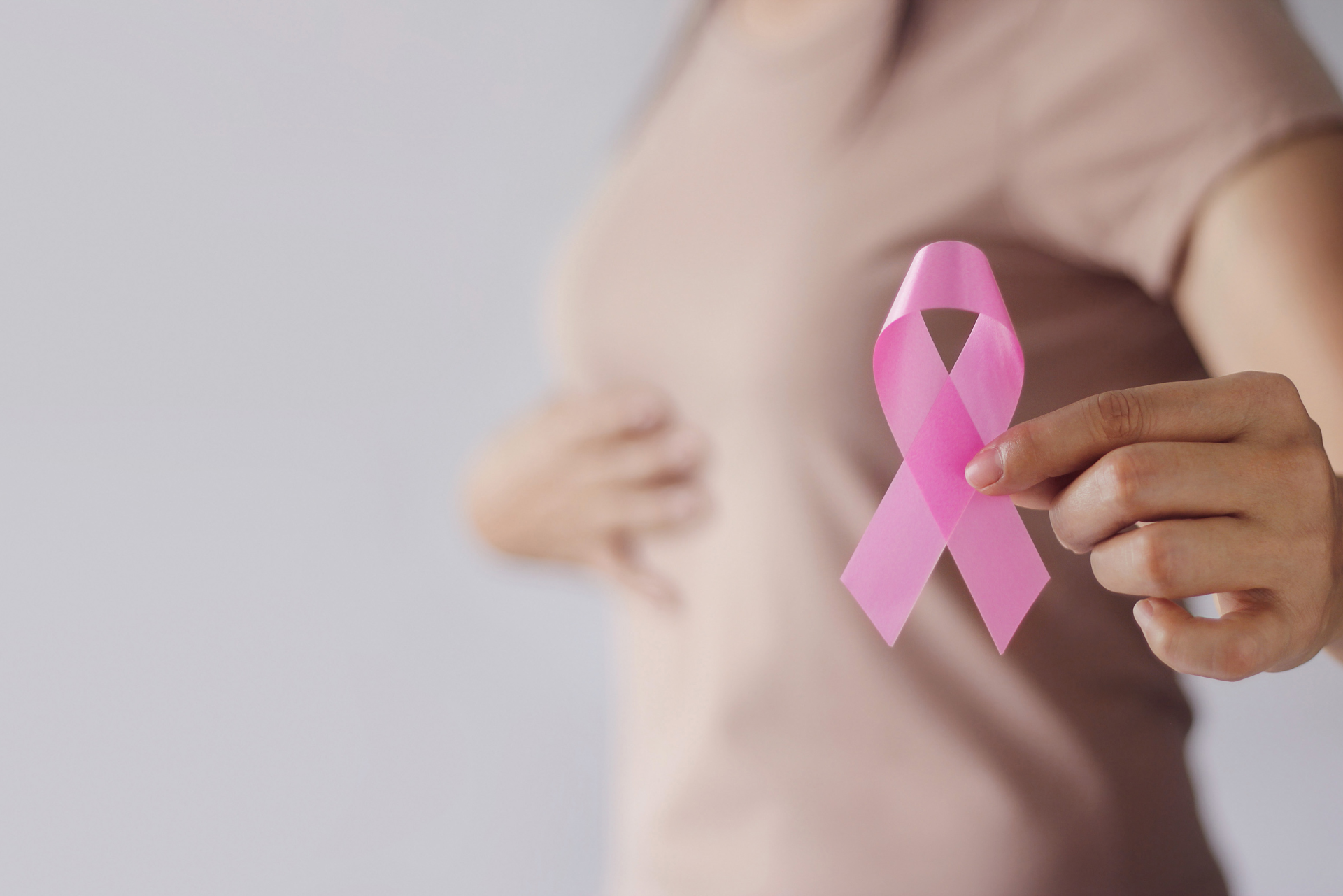 Une femme tenant un ruban rose, symbolisant la sensibilisation au cancer du sein, devant sa poitrine.