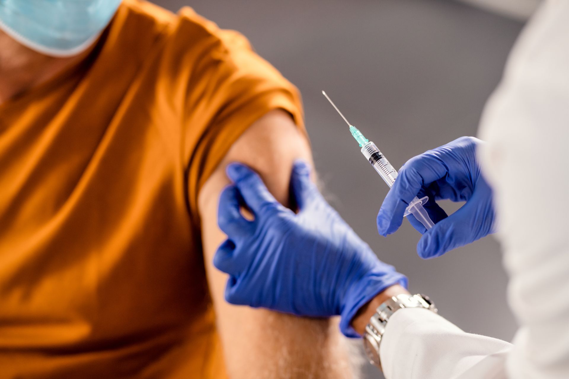 Healthcare worker giving an injection to a patient’s upper arm with a syringe and blue gloves
