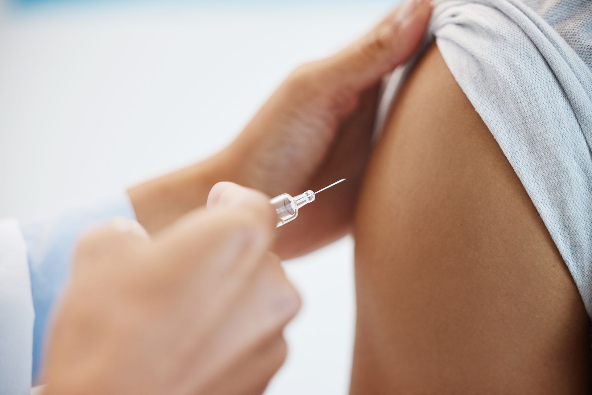 Syringe preparing to inject a person’s upper arm with a vaccine