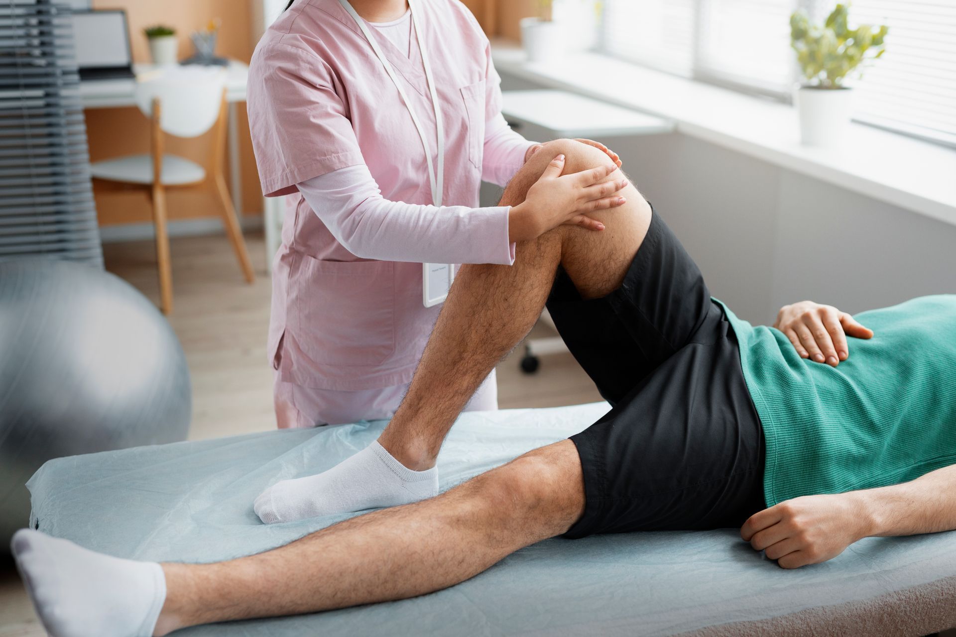 Physical therapist stretching a patient’s leg on a treatment table in a bright clinic room