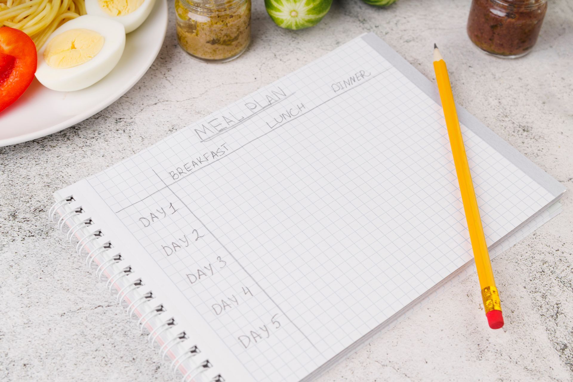 Open notebook planner with a yellow pencil and small containers on a light countertop.