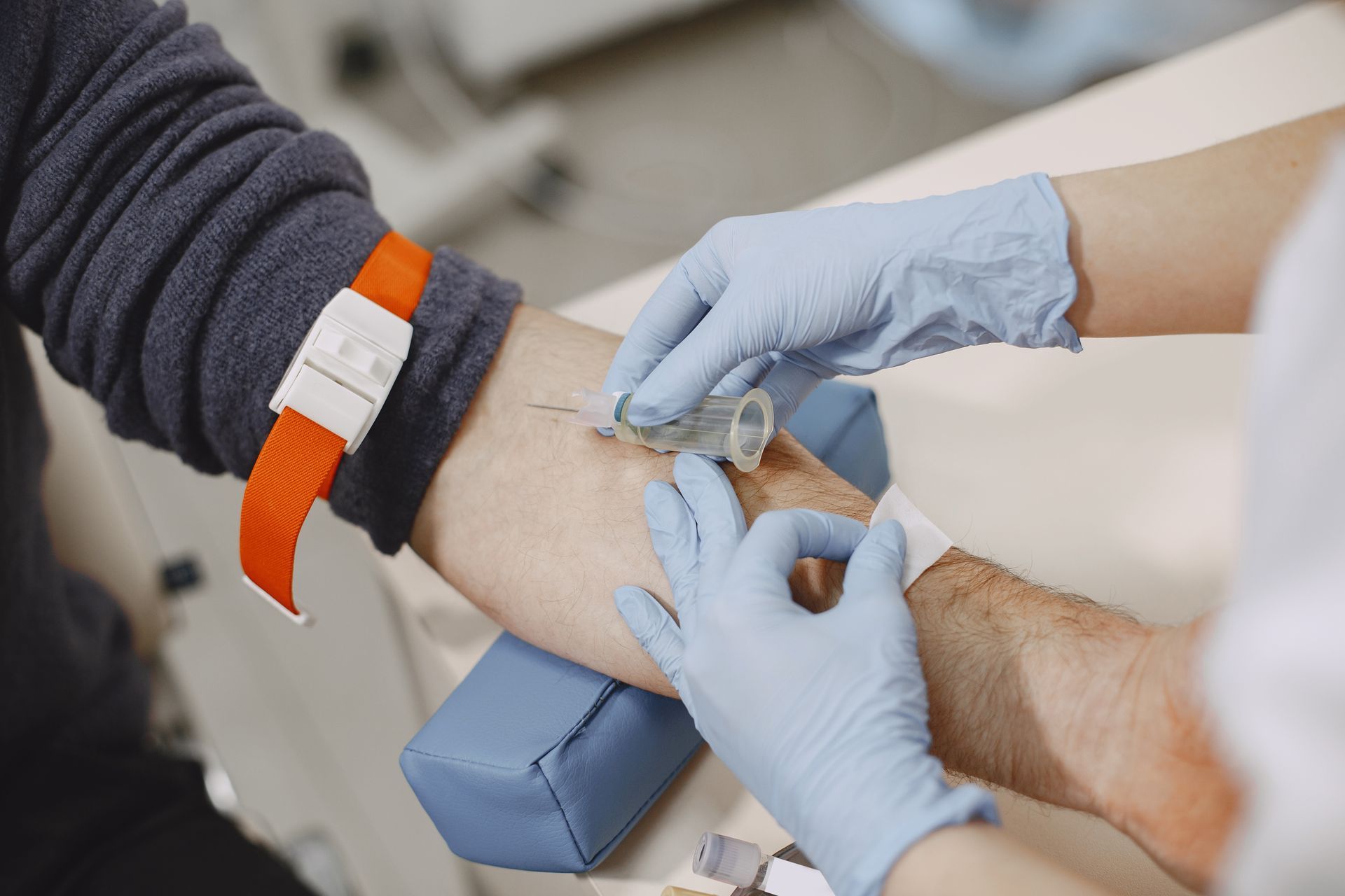 Gloved hands drawing blood from a patient’s arm with a tourniquet and vial attached