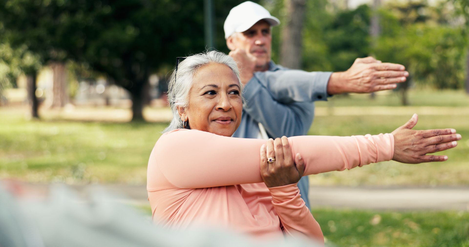 Two people stretching outdoors in a park, arms extended forward during exercise.