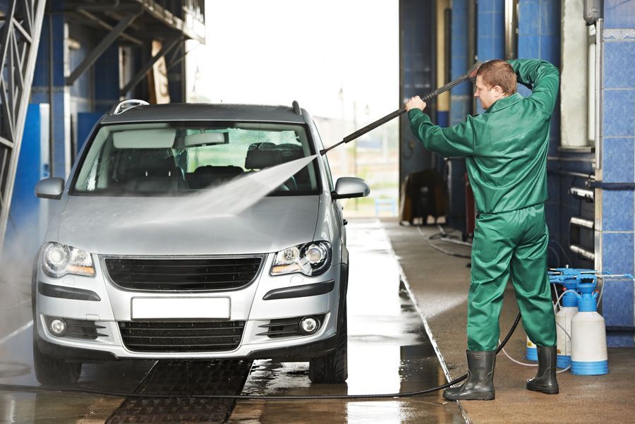 A man dressed in green uses a pressure washer to clean a car, representing Satisfy Utah.