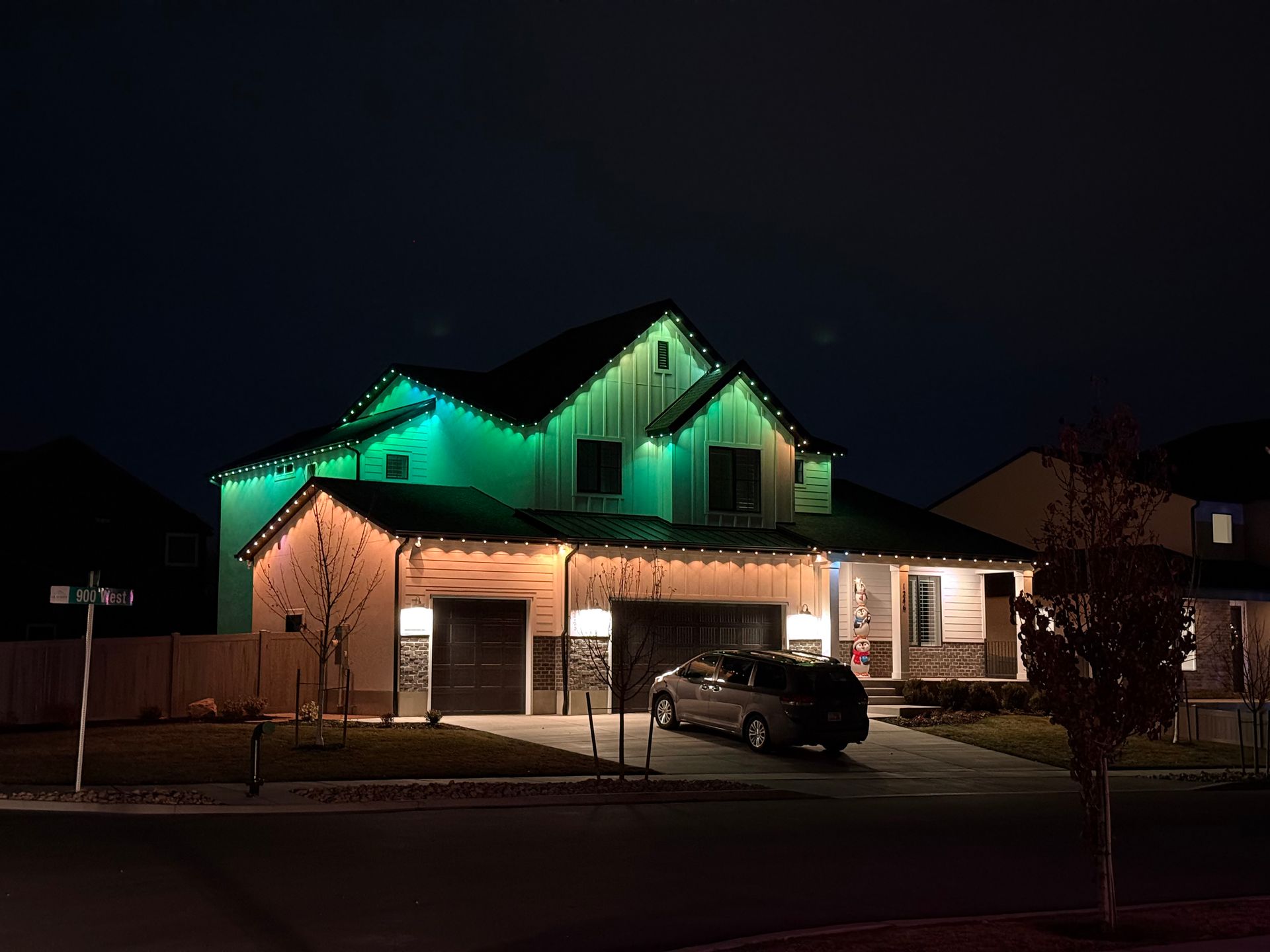Two-story house at night, with green and white lights illuminating the roof. A car is parked in the driveway, creating a cozy and serene atmosphere.