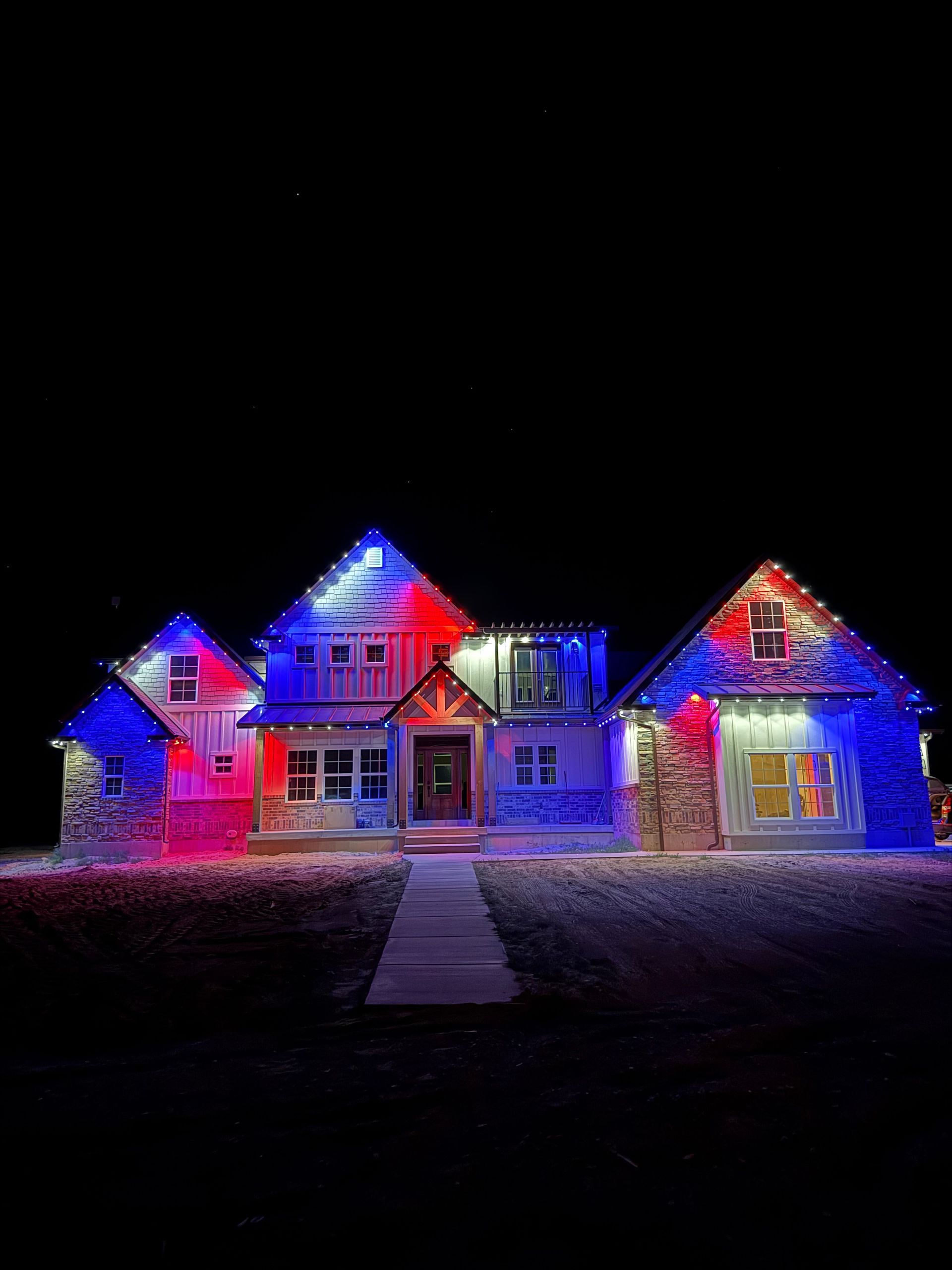 A house illuminated with vibrant red, blue, and white lights against a dark night sky. The festive lighting creates a cheerful and lively atmosphere.