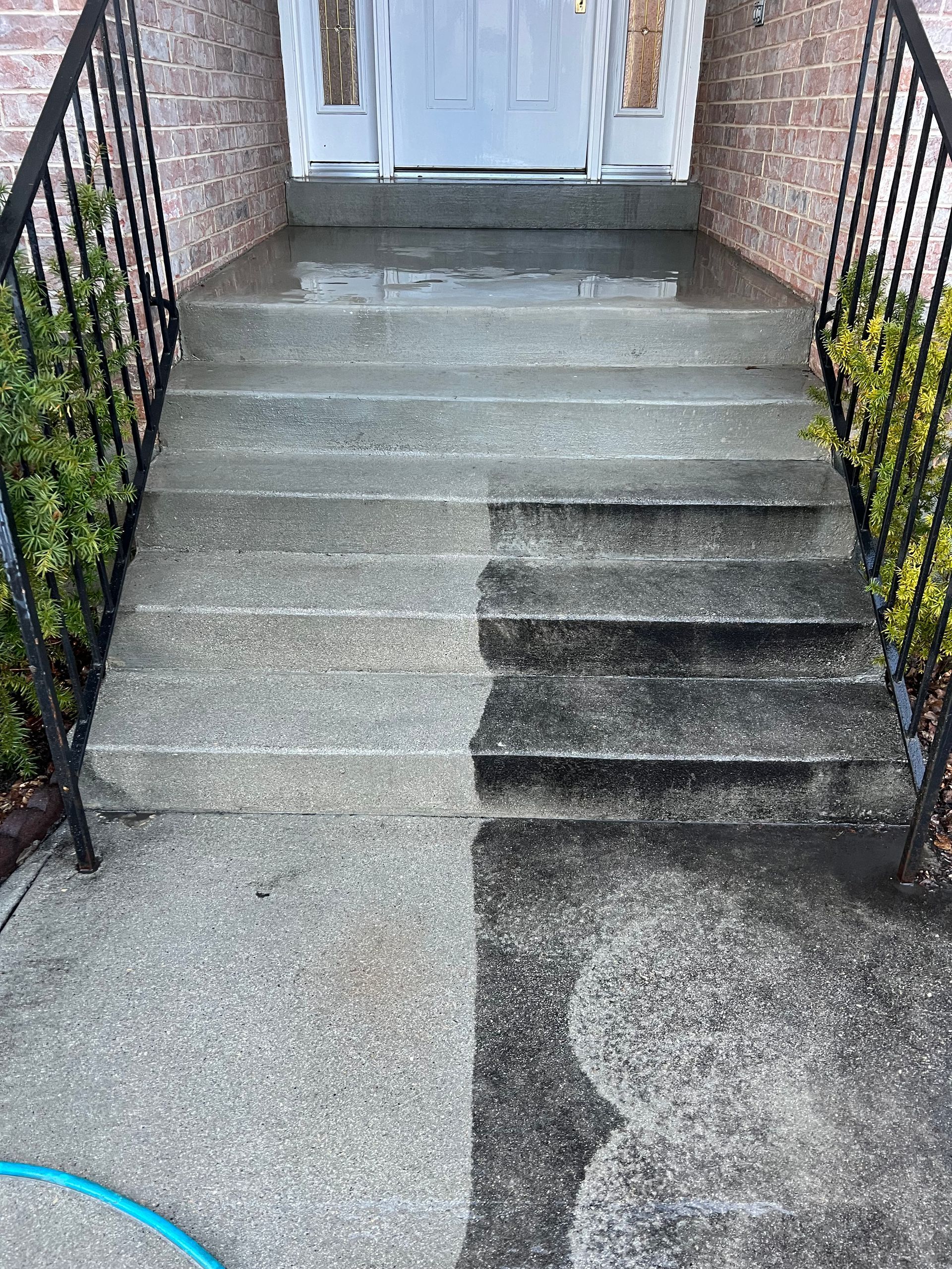 A set of concrete steps ascends to a front door, featuring a sign that says 