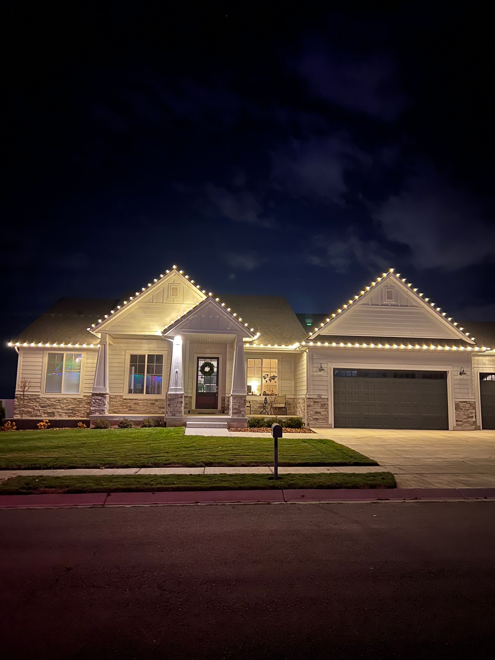 Single-story house at night adorned with glowing white string lights along the roof. The scene is calm, highlighting festive, cozy ambiance.