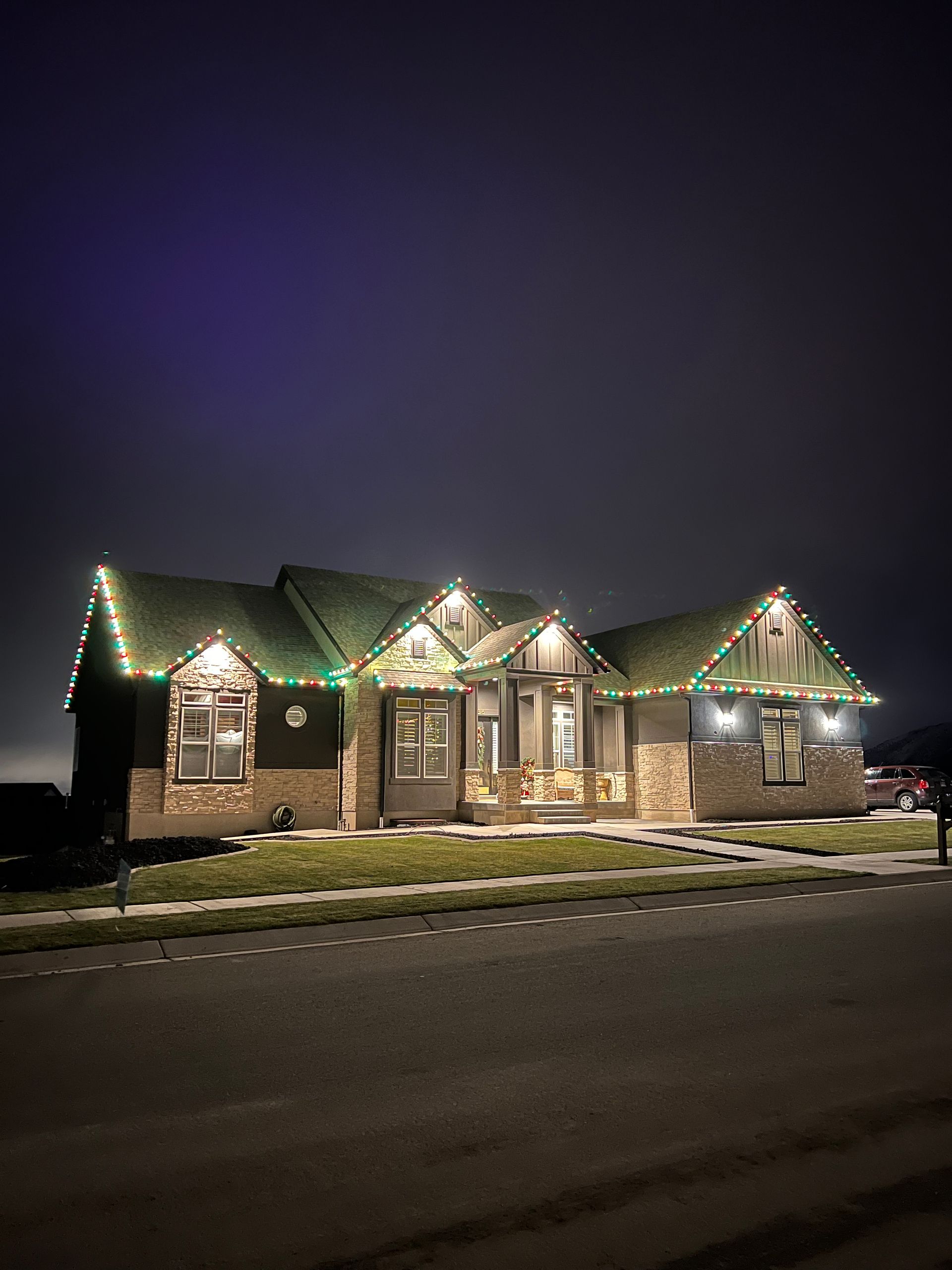 A cozy house at night is adorned with colorful holiday lights along the roofline. The warm glow creates a festive and inviting atmosphere.