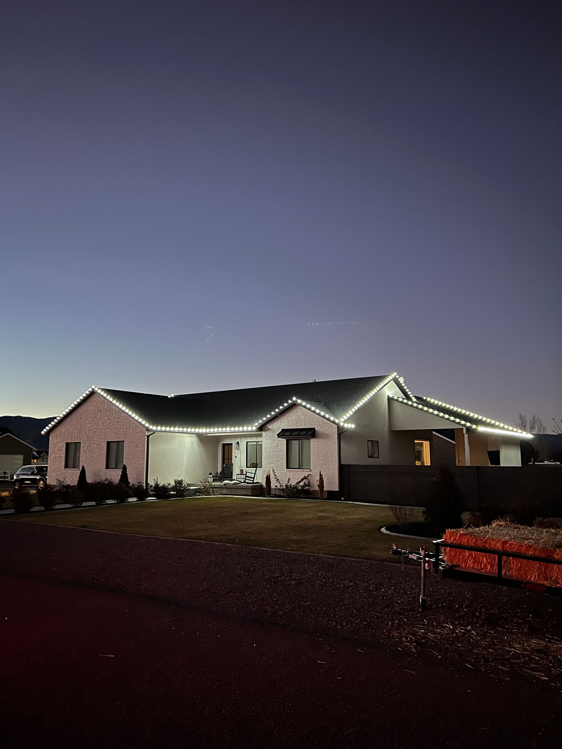 Single-story house at dusk with white string lights outlining the roof. Calm evening sky in the background adds a serene and festive ambiance.
