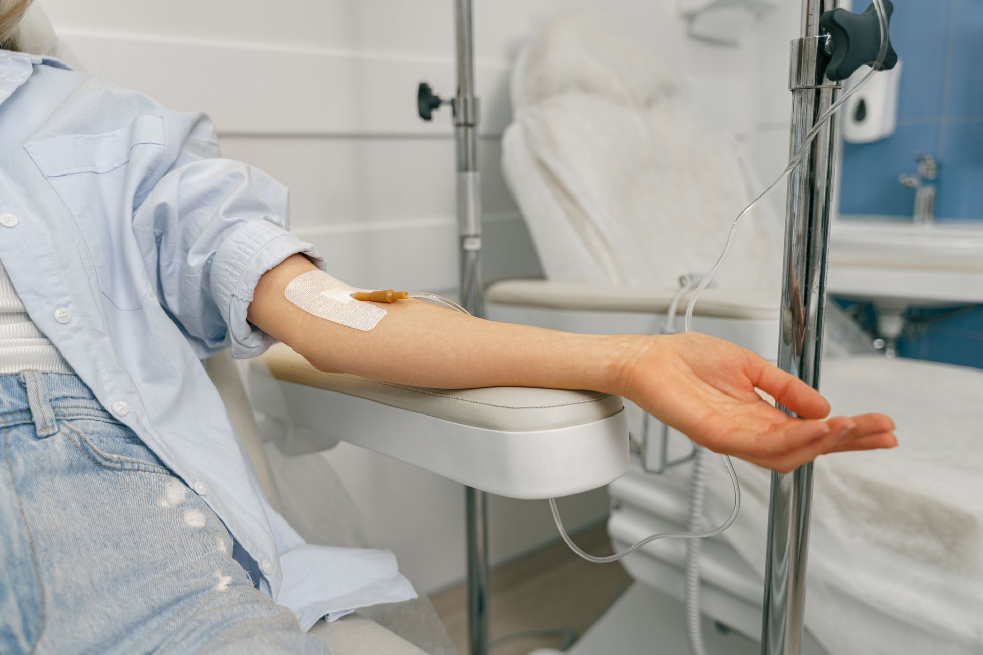 A person’s arm with an IV line and medical tape attached while resting on a medical chair in a clinic setting.