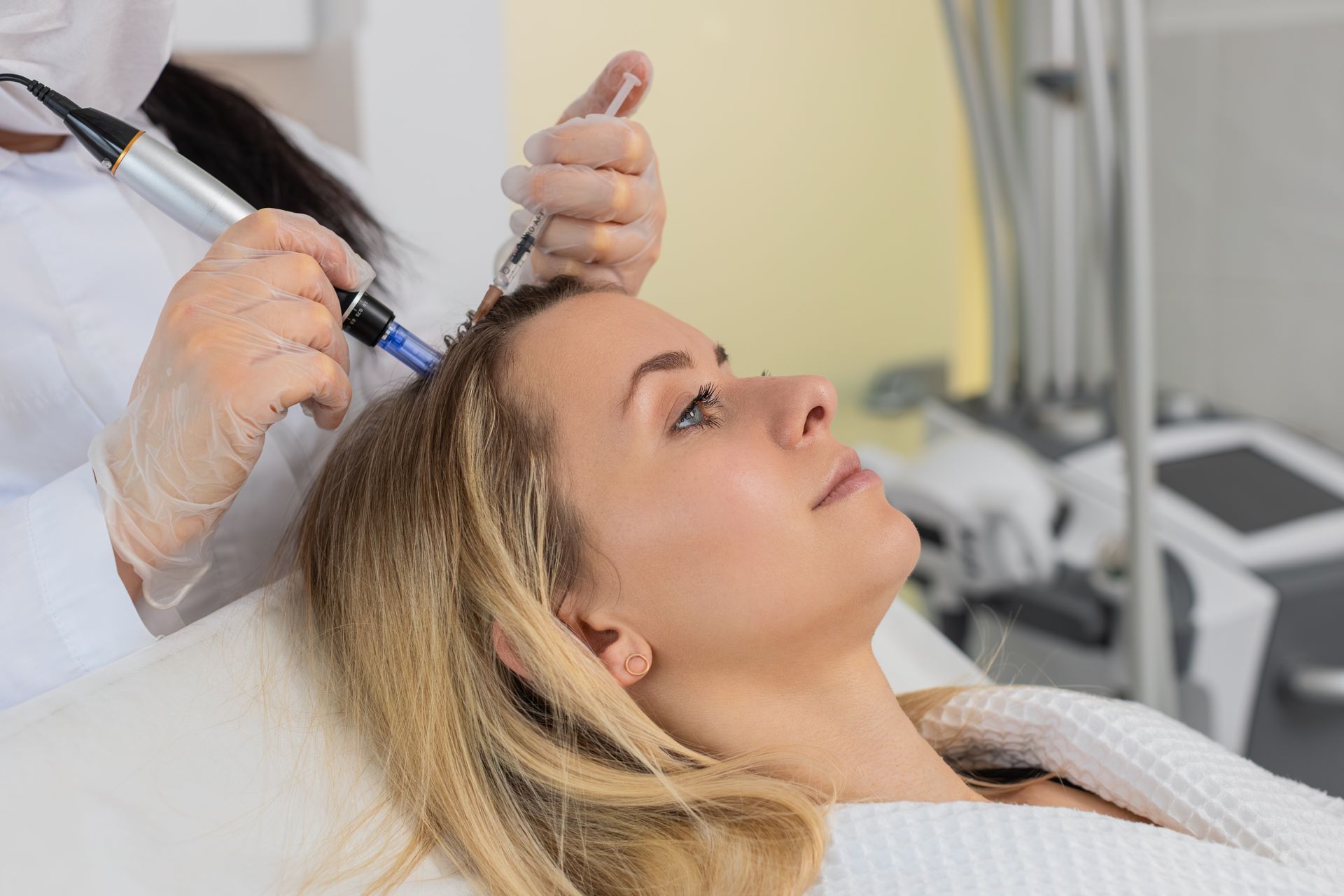 A person receiving a scalp treatment with a microneedling device from a practitioner wearing gloves in a clinic setting.