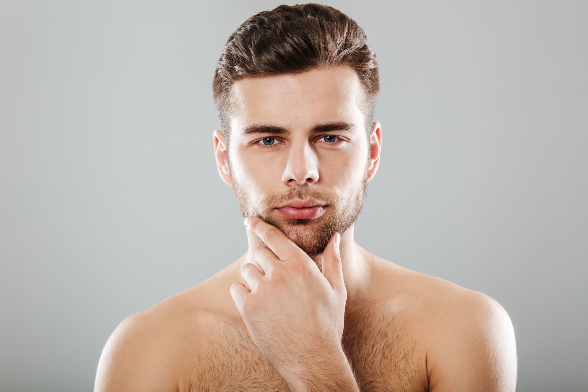 A shirtless man with a beard is holding his hand to his chin.