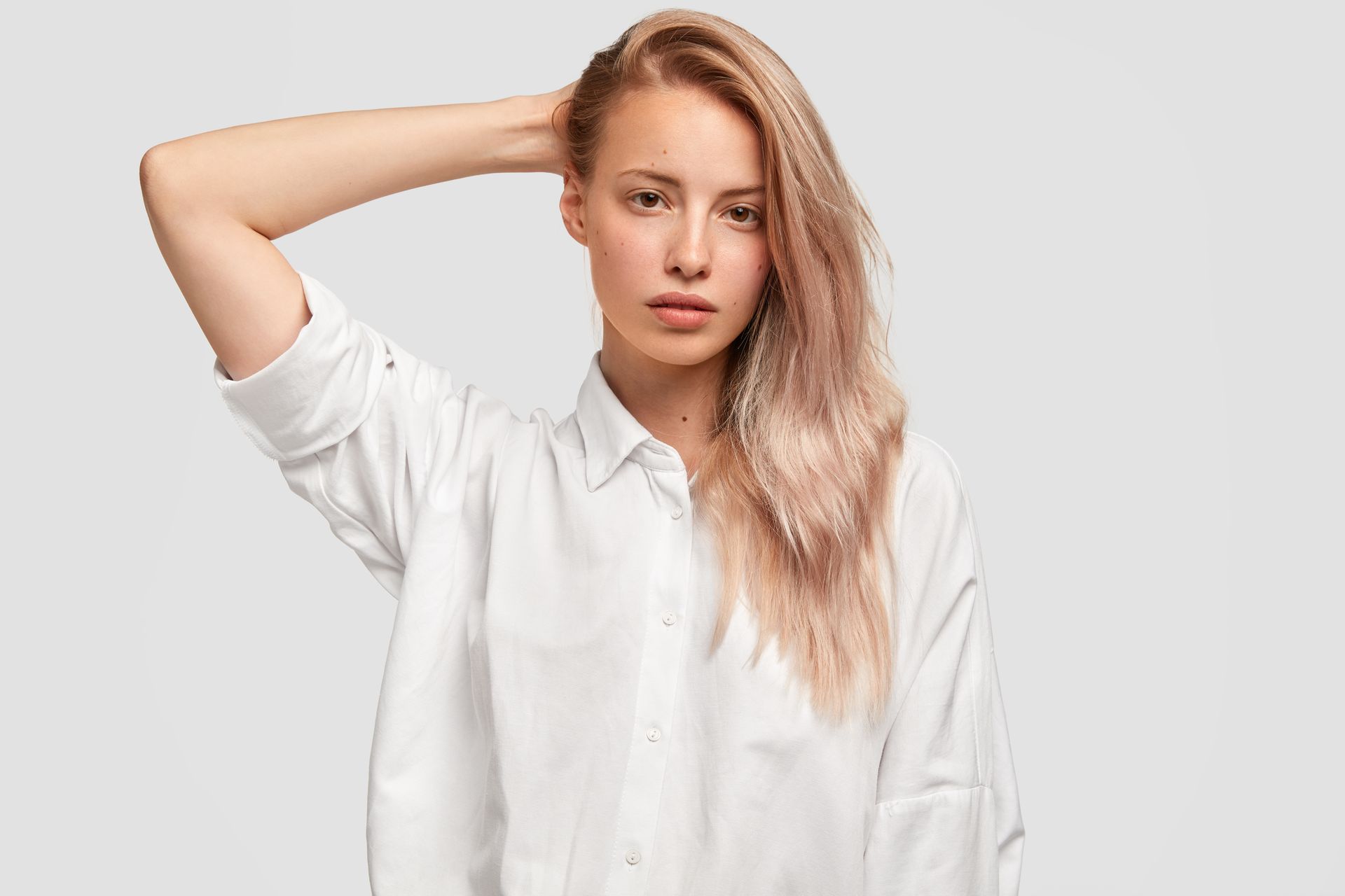 A woman in a white shirt is holding her hand to her head.