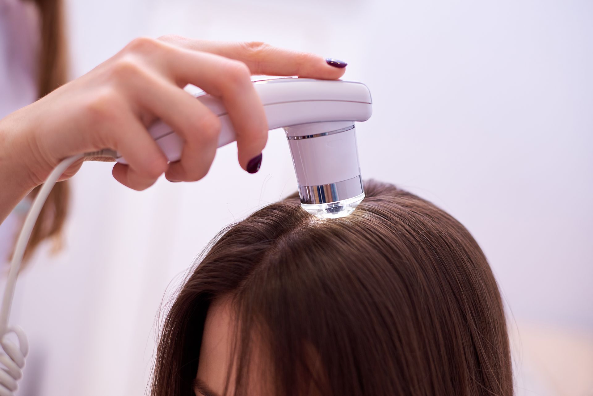Hand using an electric scalp massager on parted brown hair