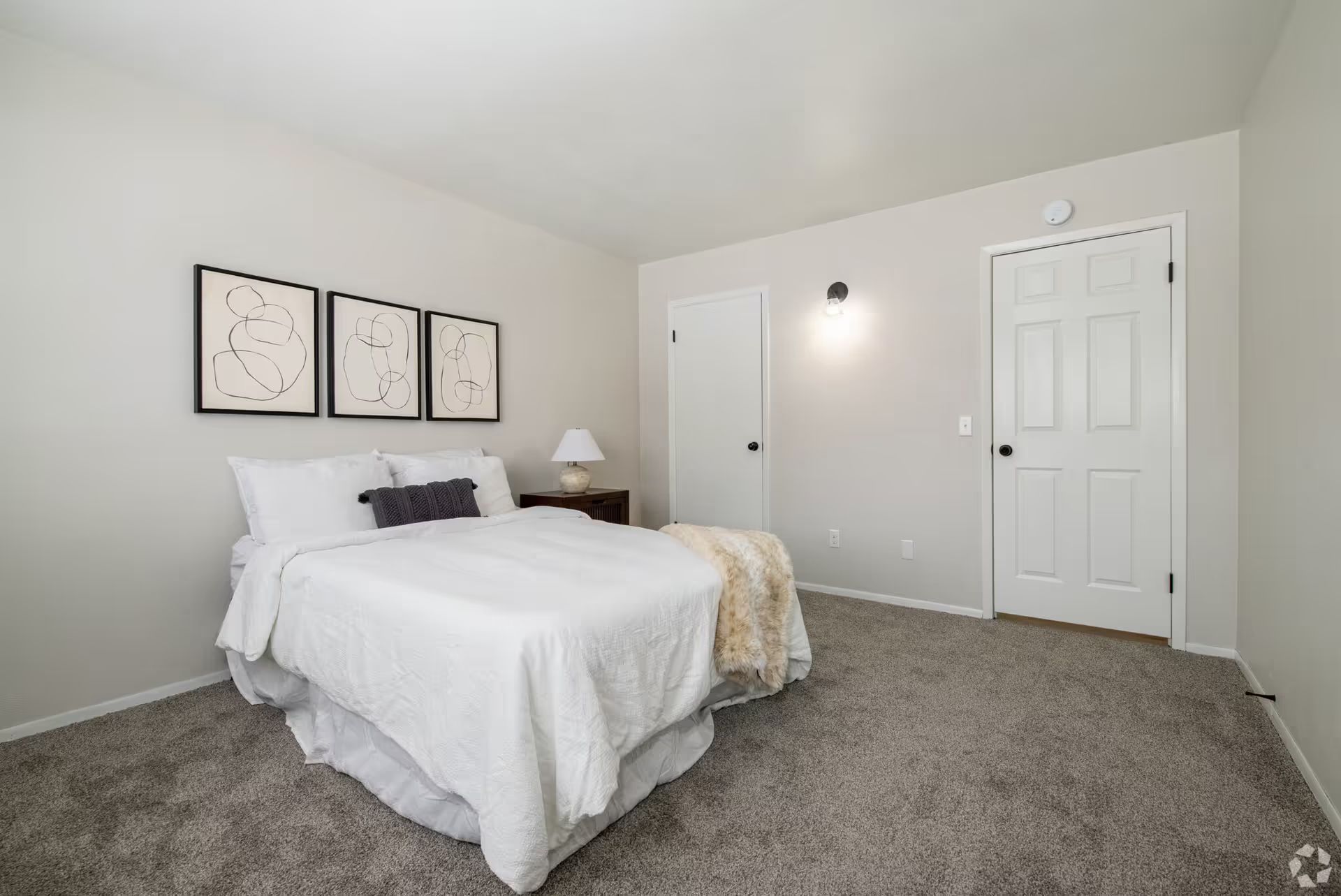 A bedroom with a bed , nightstand , lamp and carpet.