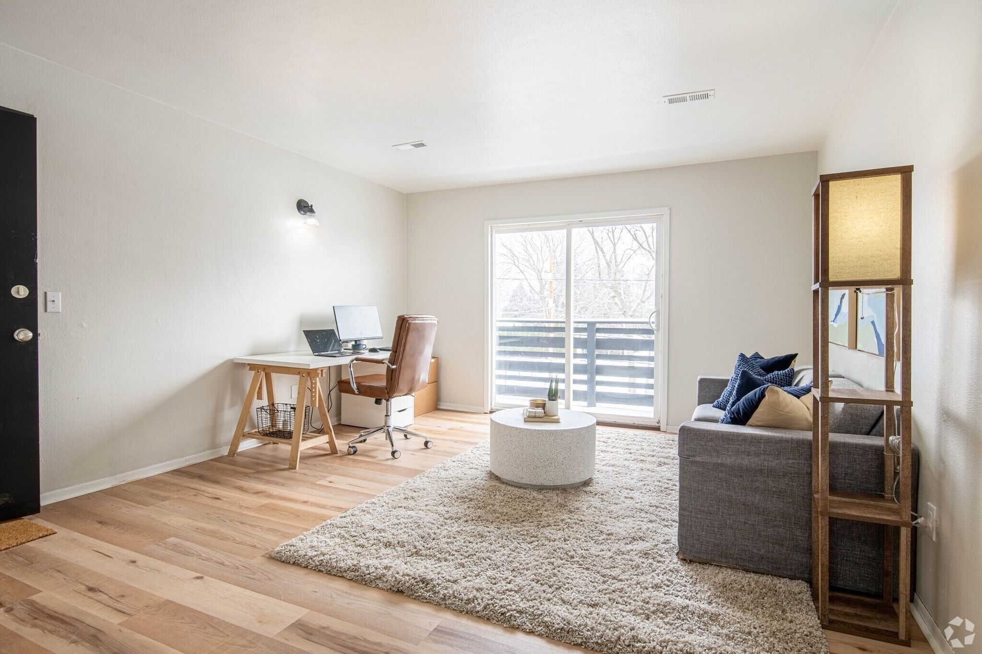A living room with a couch , desk , chair and sliding glass doors.