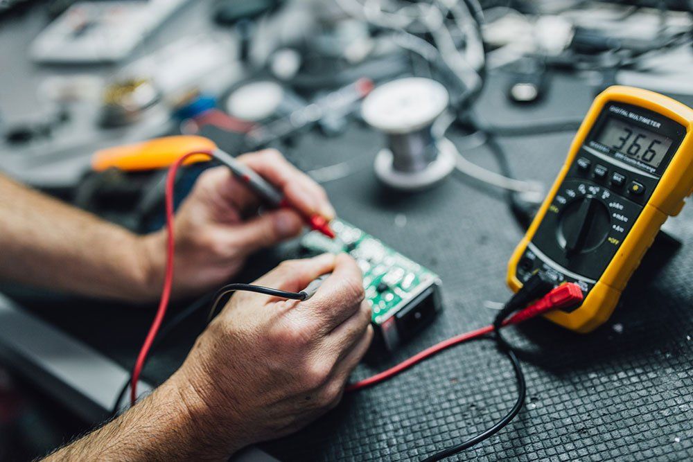 Hands Checking Board with Multimeter | Sturgis, MI | Prime Quality Electric, LLC