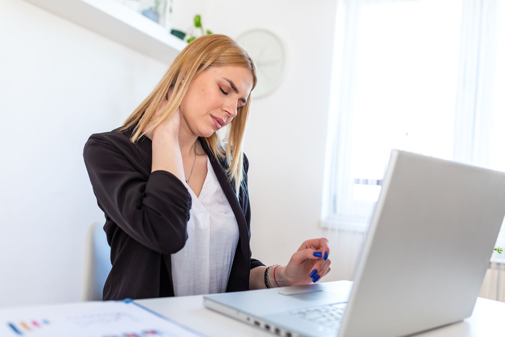 Woman sitting at a desk, talking on a phone beside a laptop in a bright office