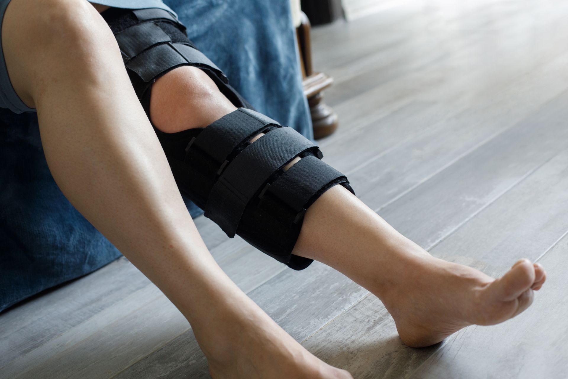 Person sitting on a floor with a black knee brace on one leg and a leg cast in the background