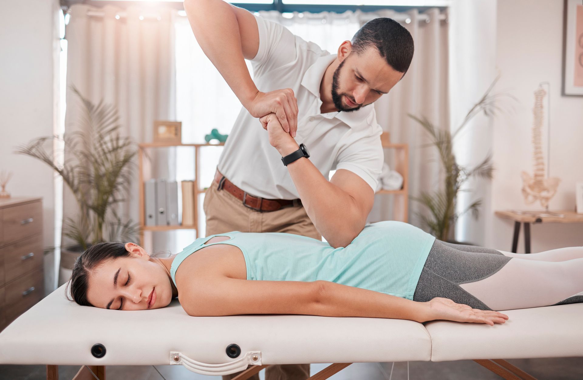 Massage therapist stretching a client on a table in a bright spa room