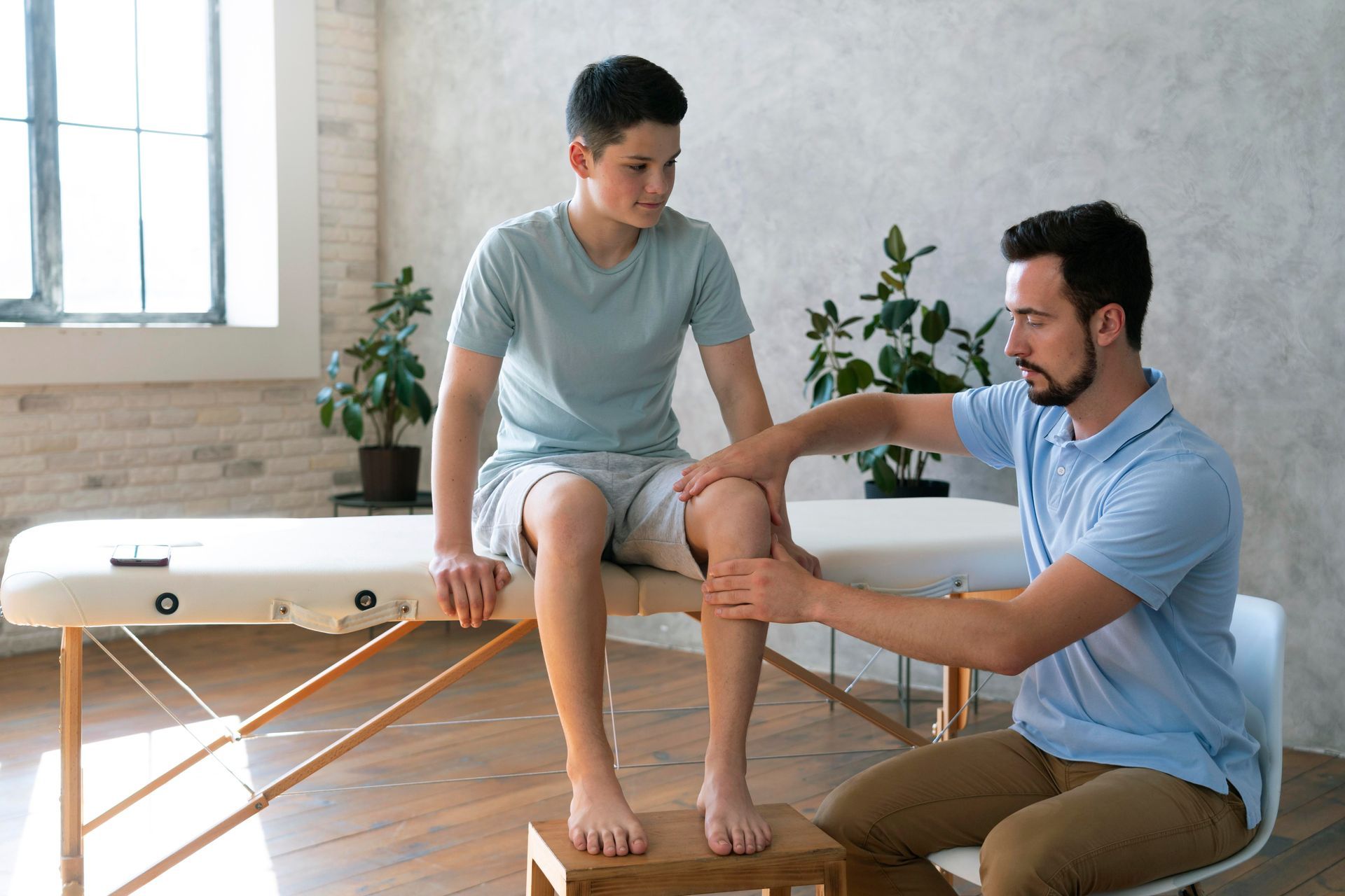 Physical therapist helping a patient stretch his leg on a treatment table in a bright clinic room