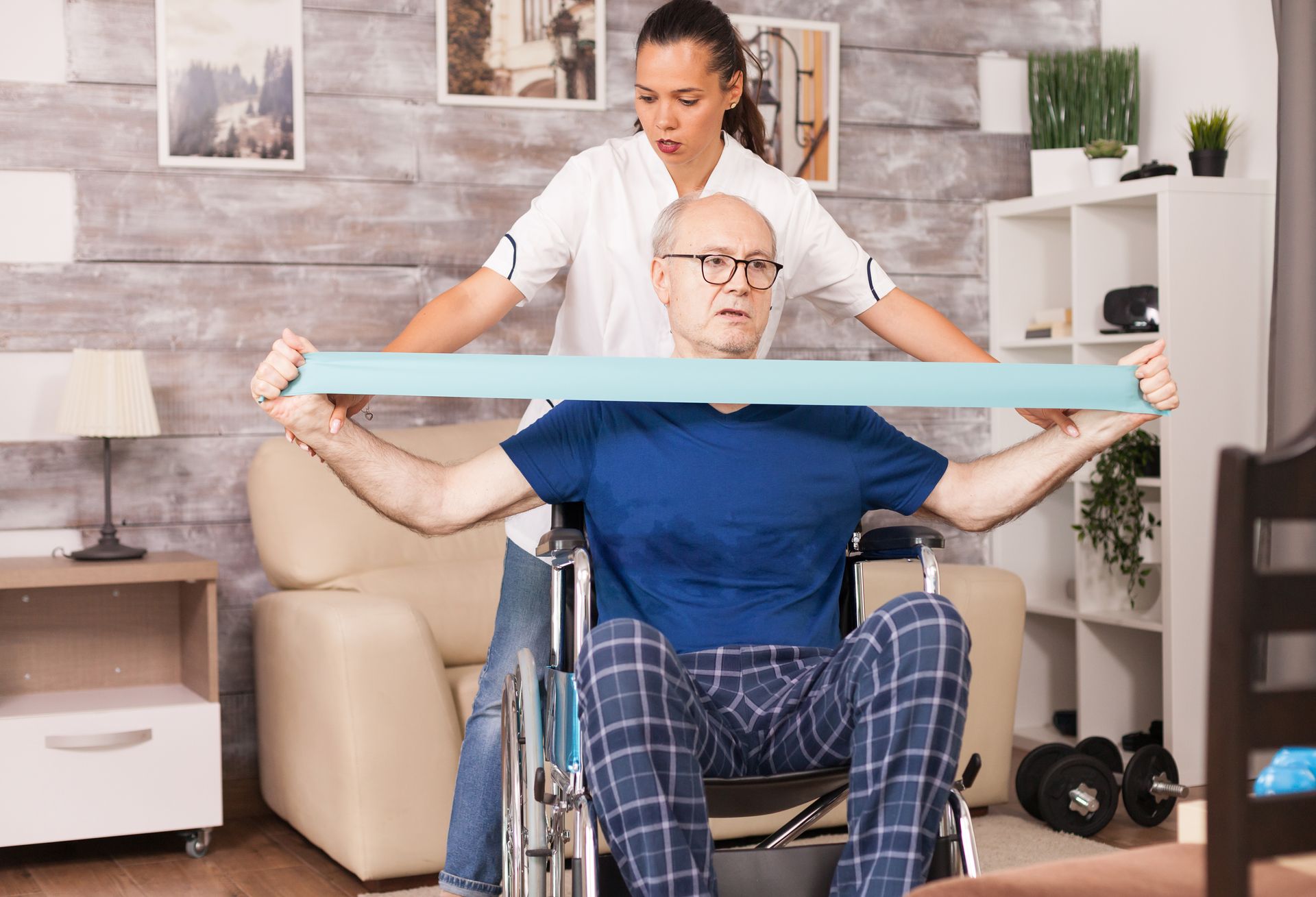 Caregiver assisting a man in a wheelchair with resistance band exercise in a living room