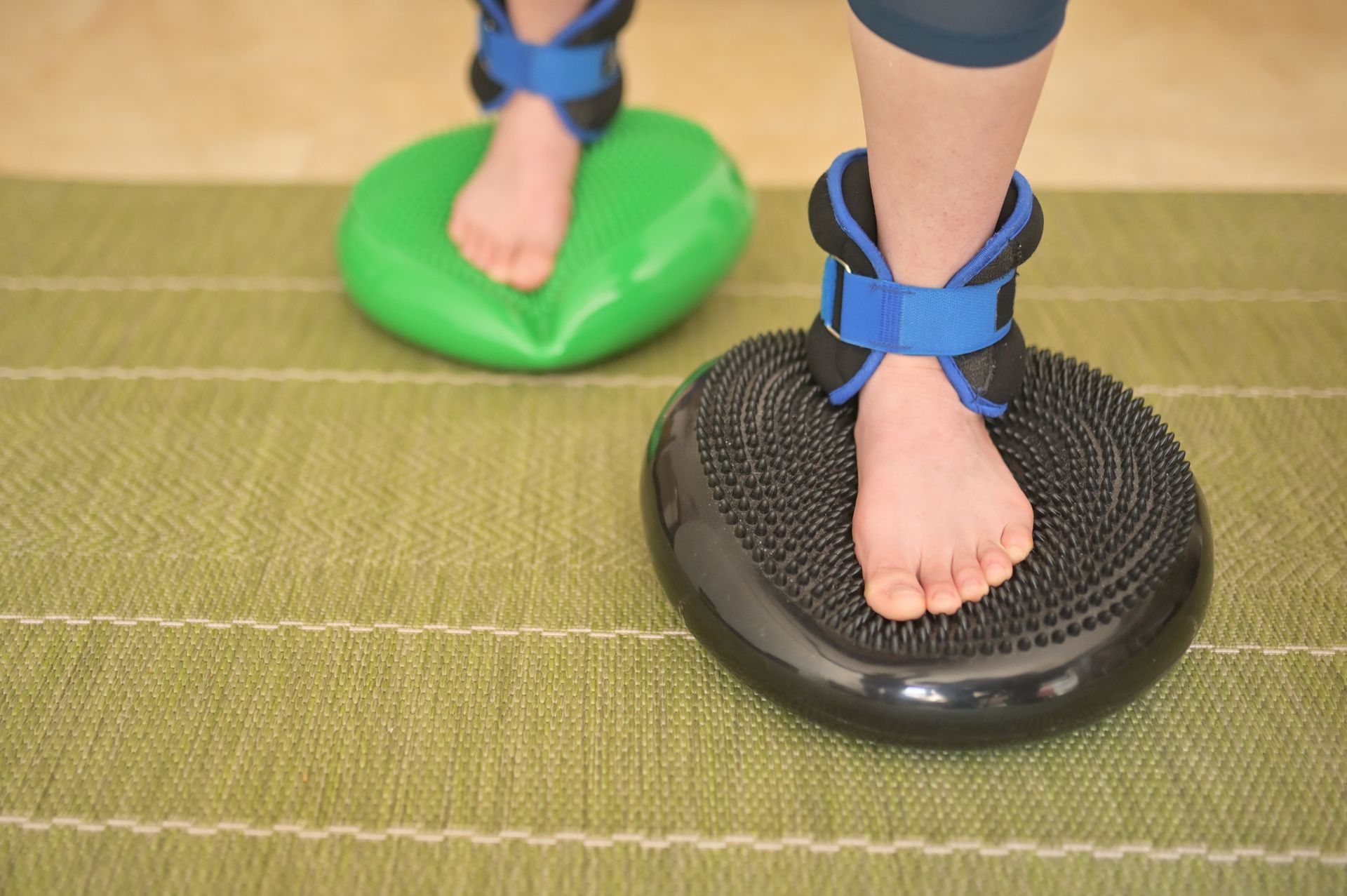 A person is standing on a balance cushion with weights on their ankles.