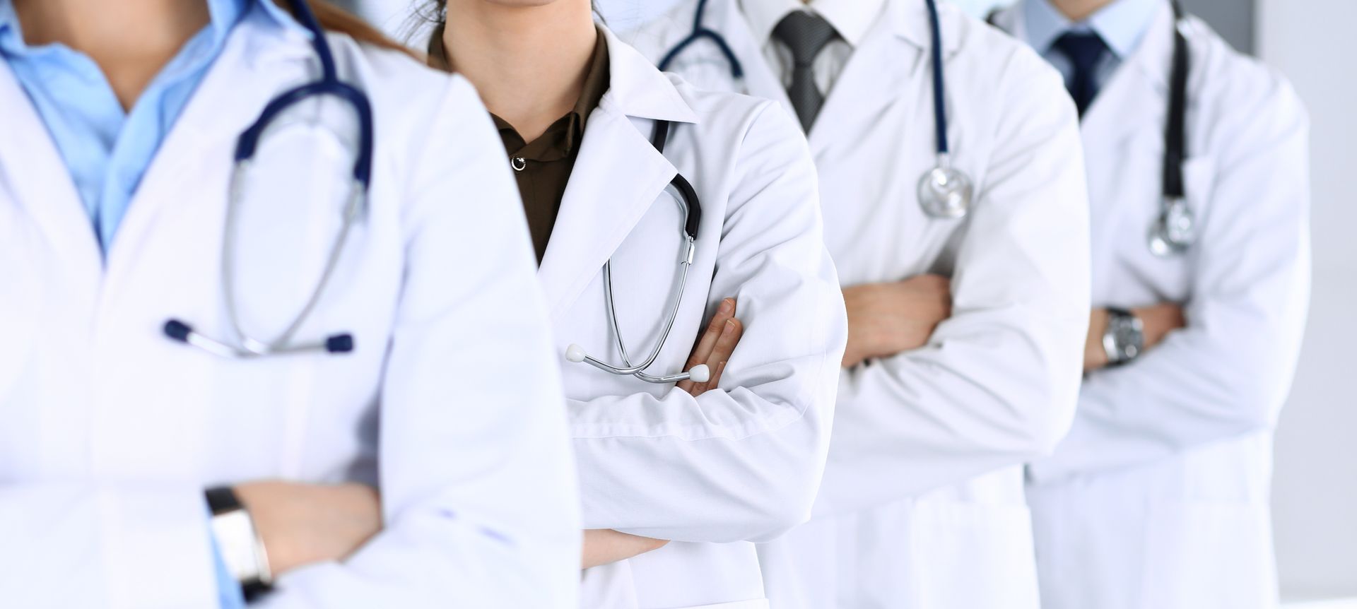 Group of physicians in white coats with stethoscopes standing with arms crossed Group of physicians in white coats with stethoscopes standing with arms crossed
