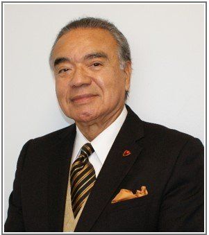 Man in a black suit and striped tie posing against a plain white background.
