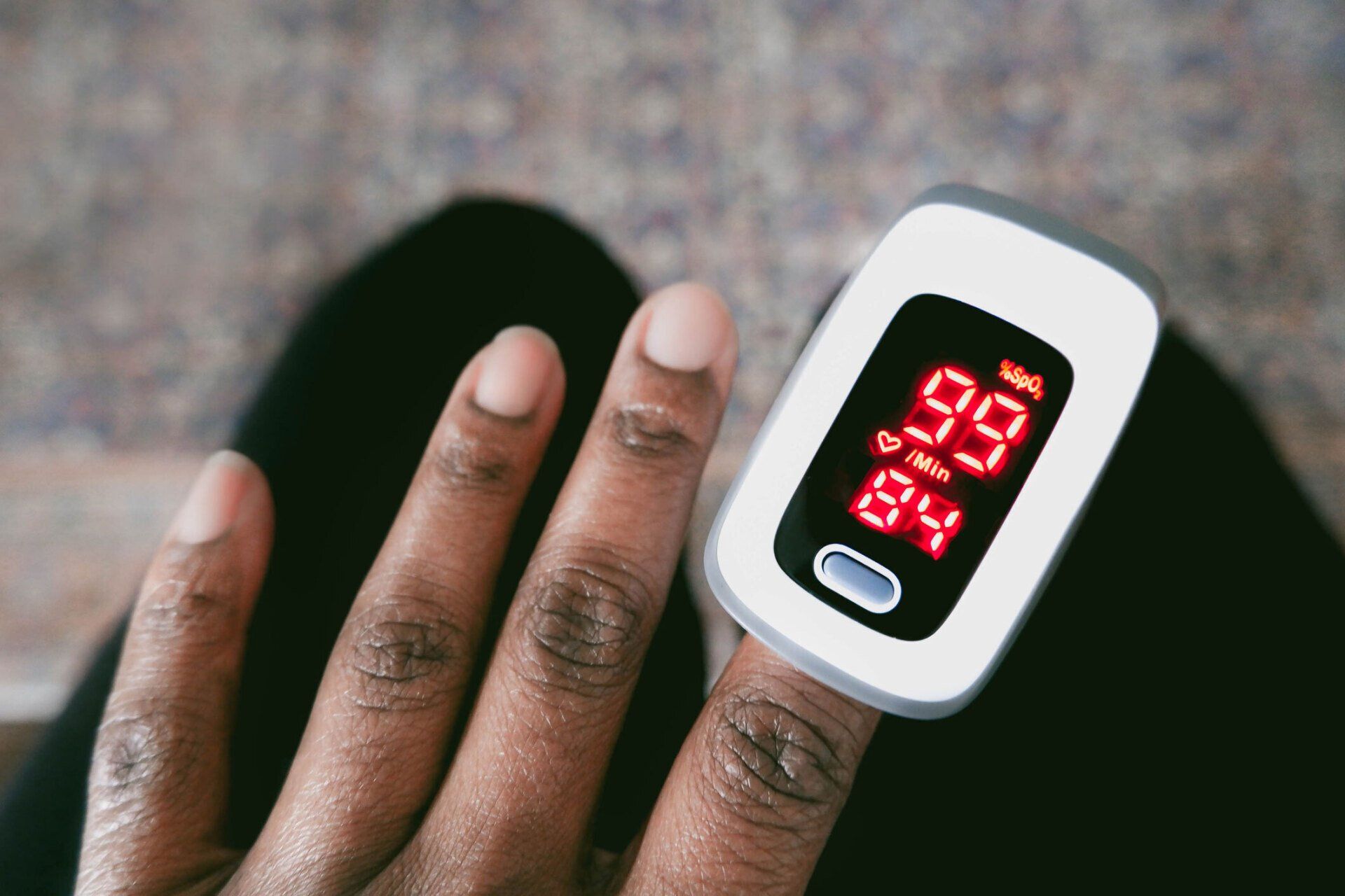 Hand with fingertip pulse oximeter showing red oxygen and pulse readings