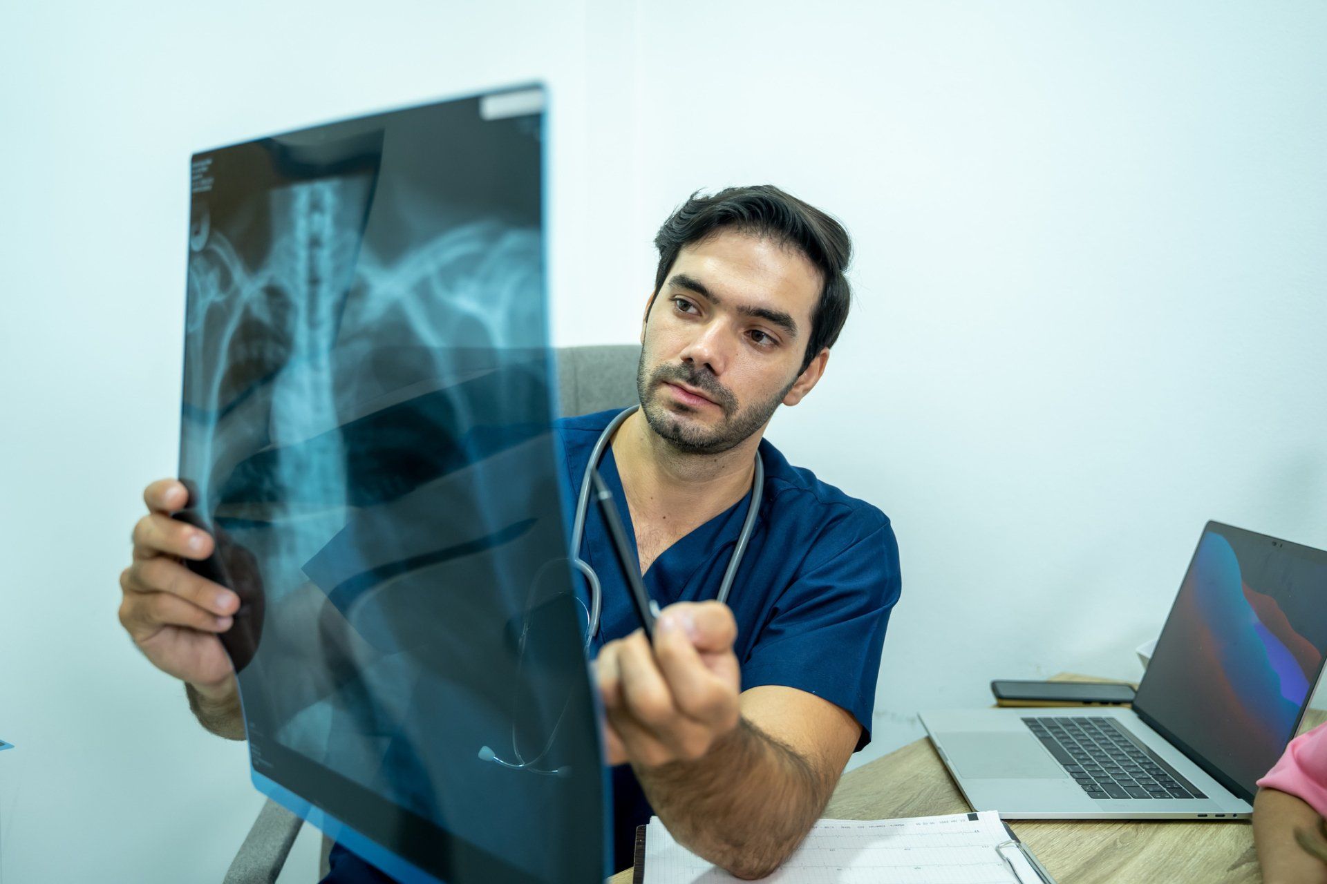 Doctor reviewing a chest X-ray beside a laptop in a medical office