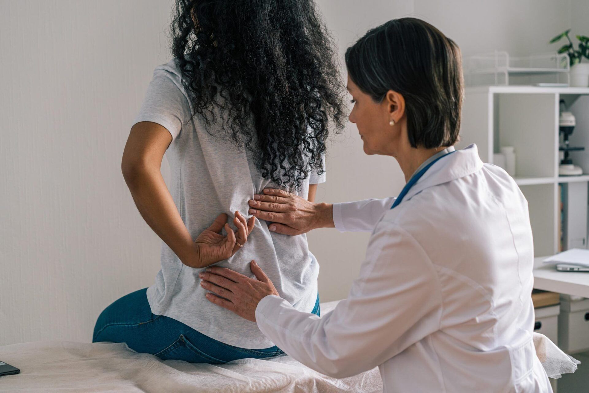 Doctor examining a patient’s back on a treatment table in a clinic room