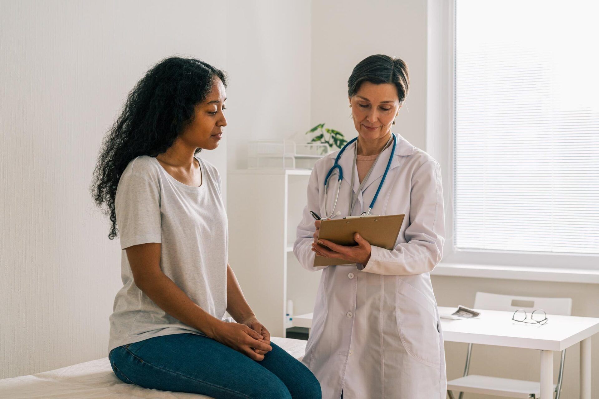 African American Female Patient Visiting Doctor — Costa Mesa, CA — Affiliated Medical Evaluators, Inc. Doctor consulting with a seated patient in a bright exam room