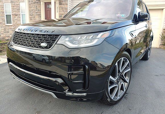 Black Land Rover Discovery SUV parked on a paved driveway in front of a house.