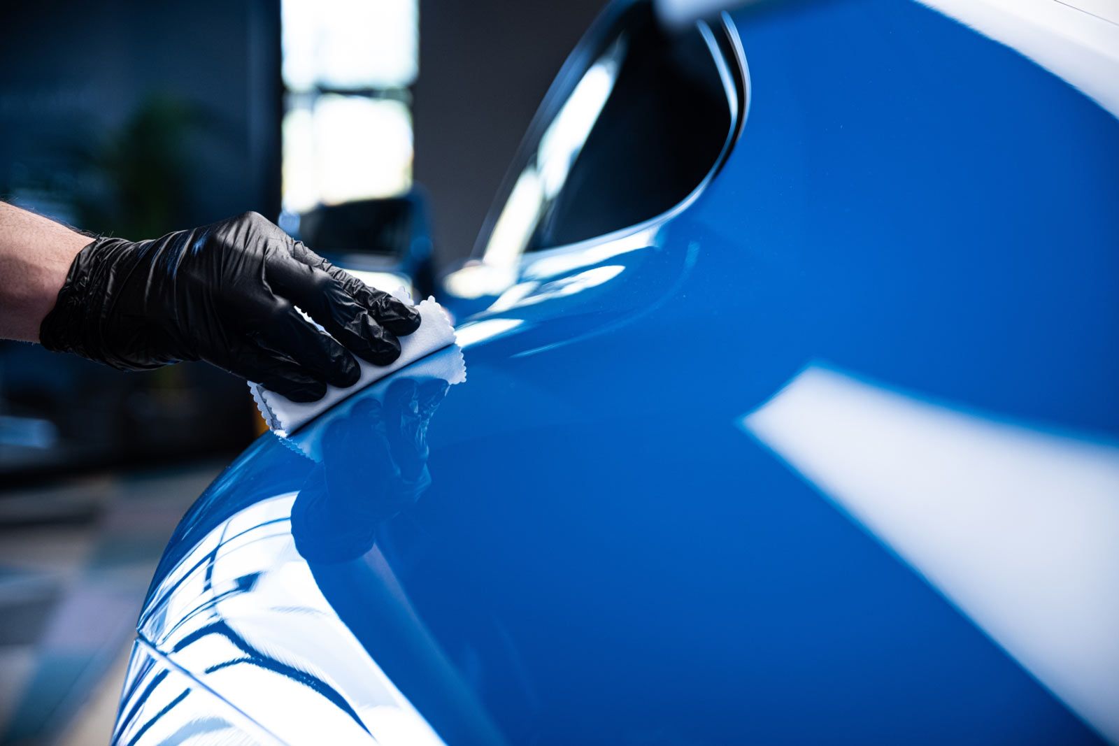 Person in black glove applies sealant to blue car's glossy surface.