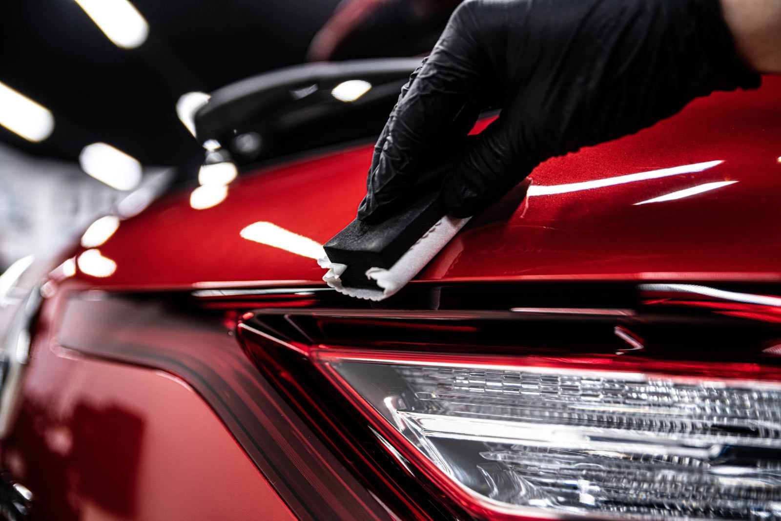 Gloved hand applying ceramic coating to a red car's hood.