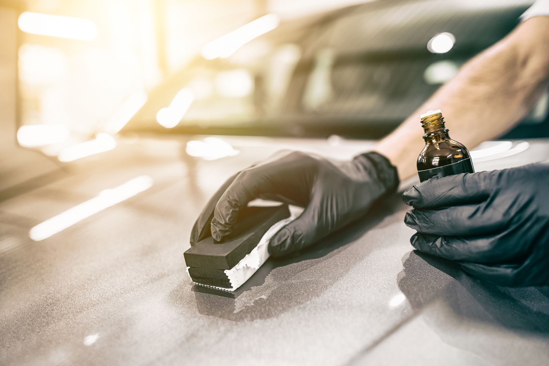 Person wearing gloves applying ceramic coating to a car's surface.