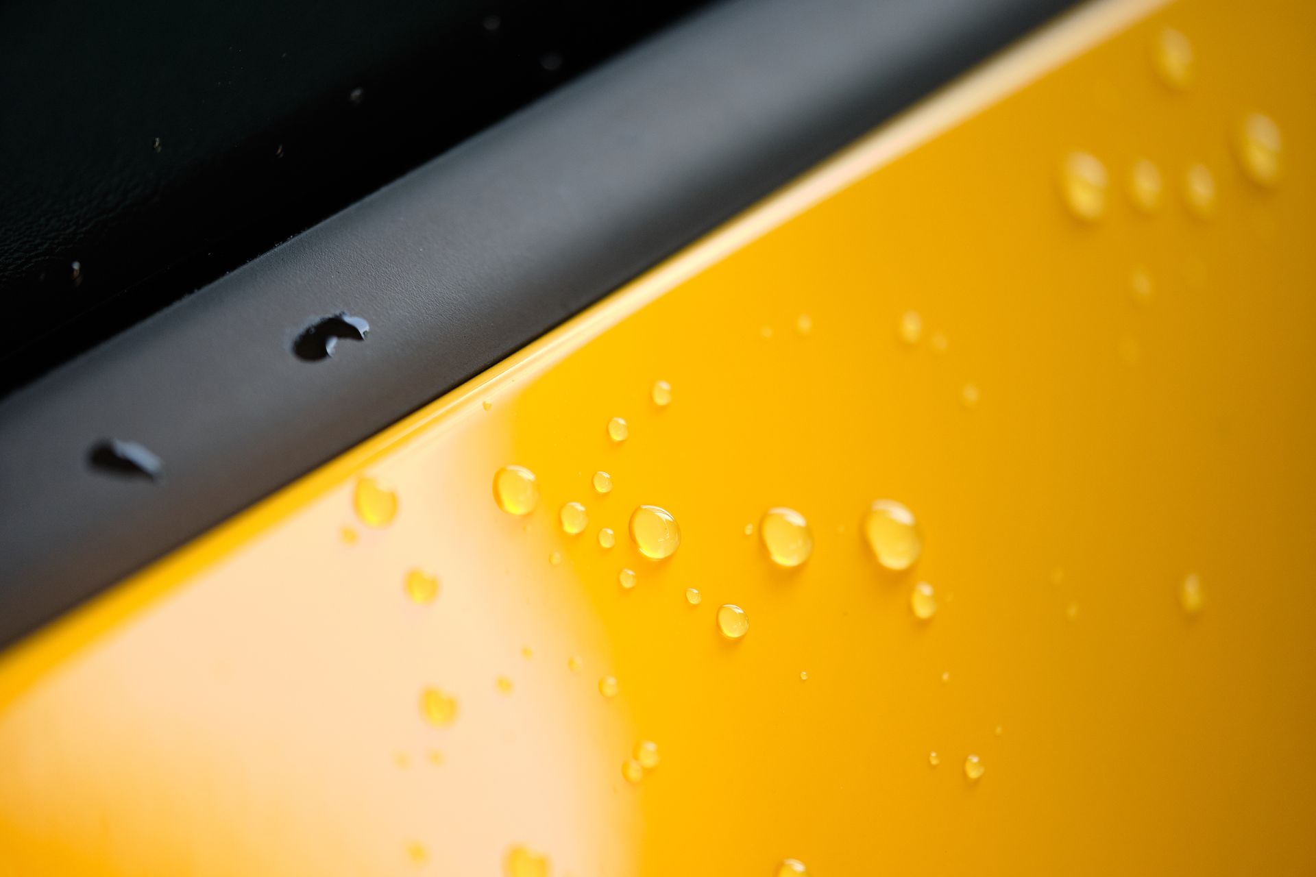 Yellow car panel with water droplets, black trim visible.