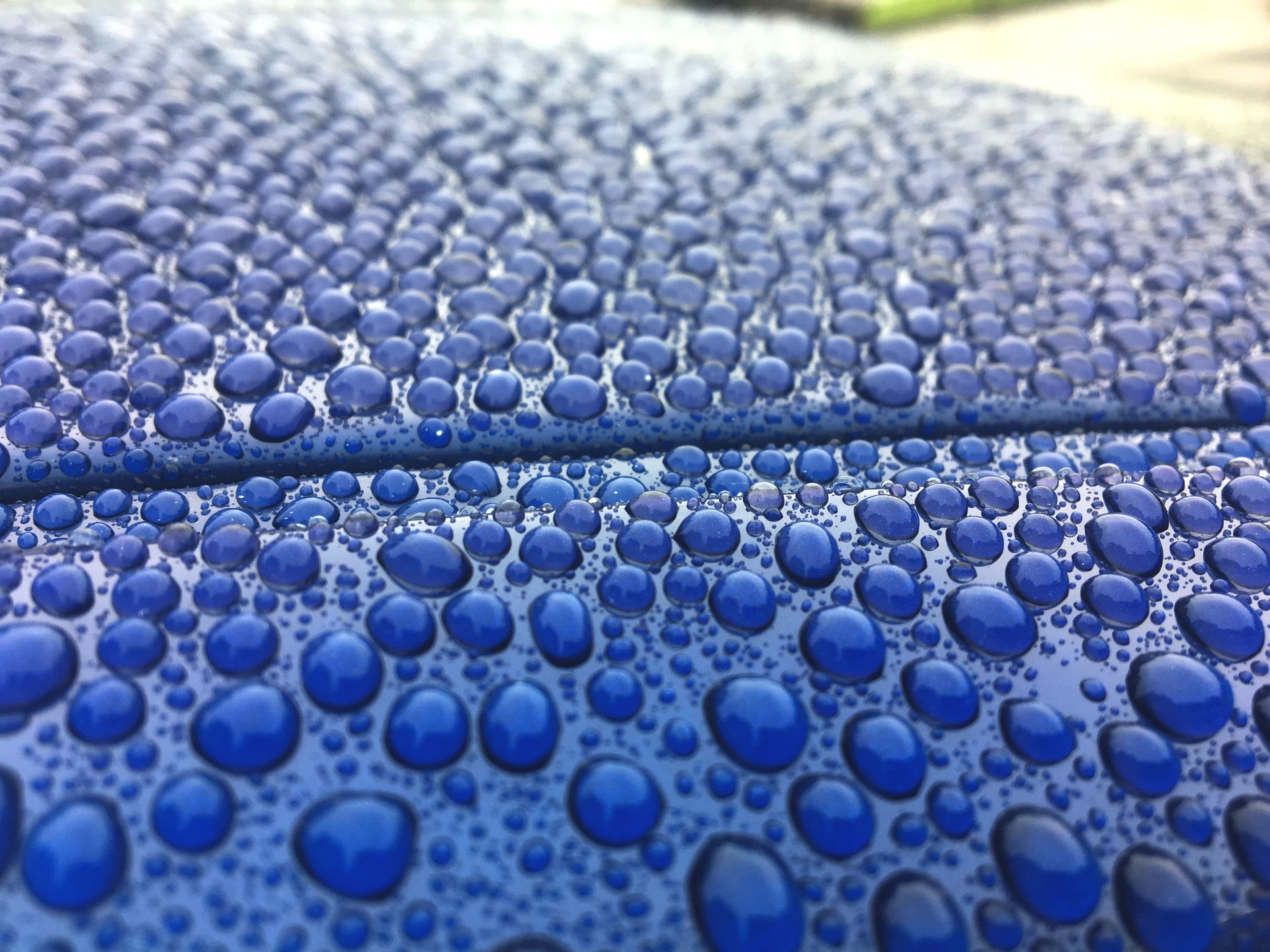Close-up of blue car surface covered in many water droplets.