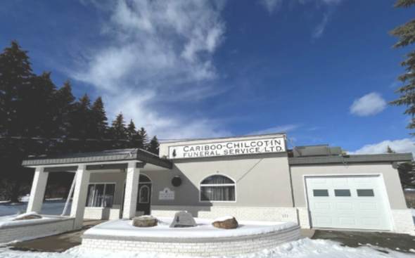 Snow-covered white building with a garage, arched window, and sign under a blue sky with clouds