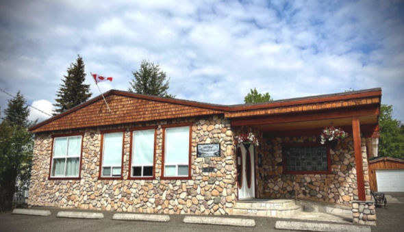 Stone building with wood roof, large windows, and a Canadian flag under a cloudy sky