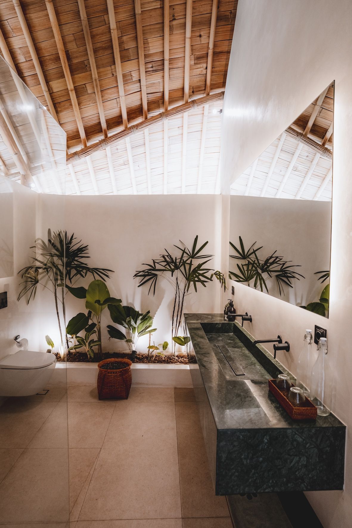 Bright restroom with plants, stone sinks, wall mirrors, and a wooden vaulted ceiling