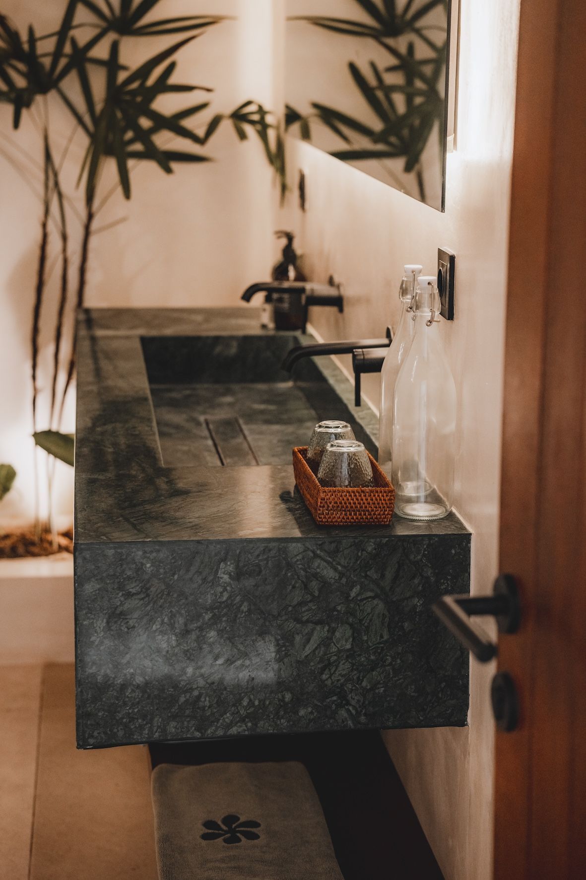 A narrow stone sink with faucet and soap dispenser in a warm-toned bathroom alcove