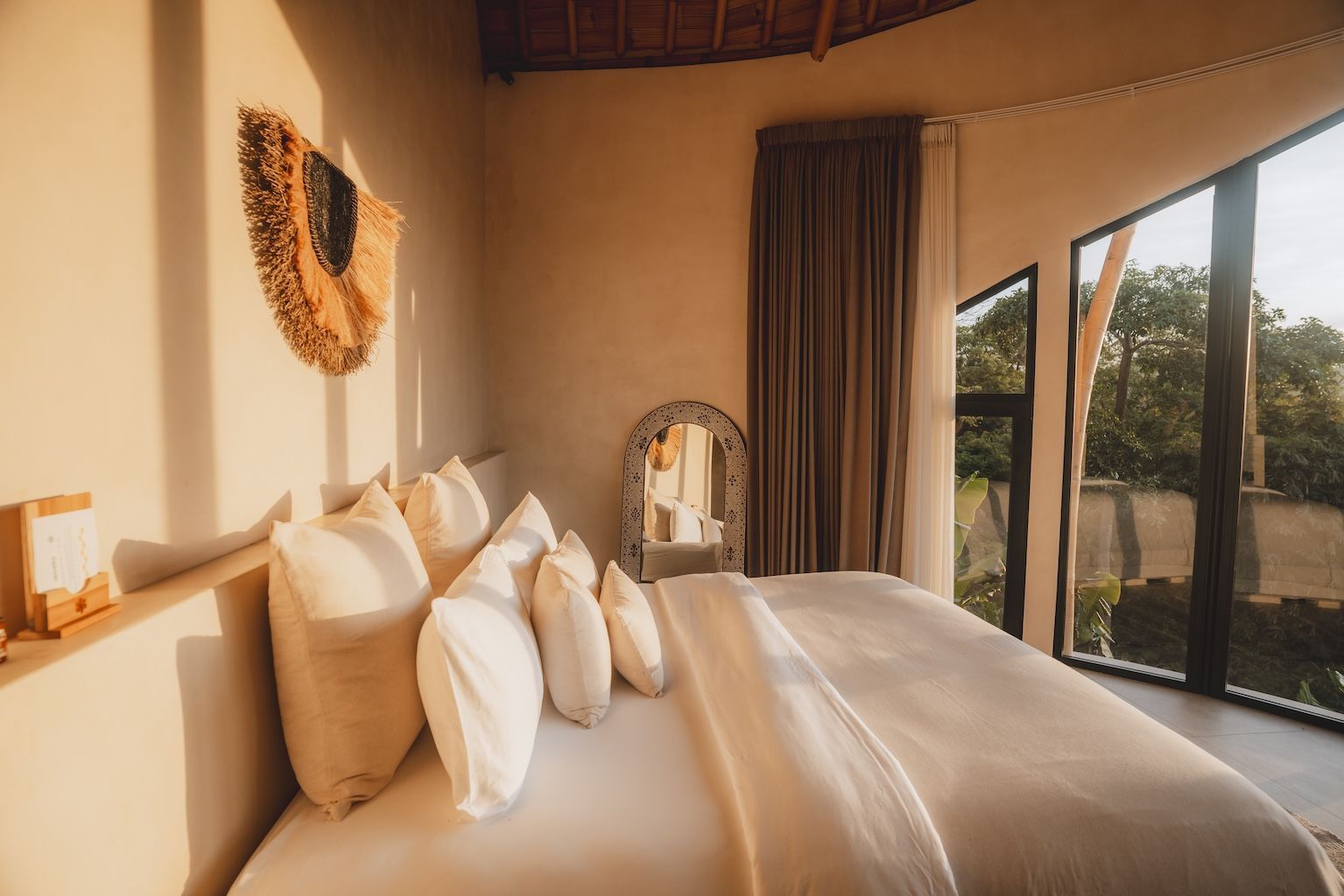 Cozy bedroom with a large bed, white pillows, woven wall decor, and a floor-to-ceiling window view