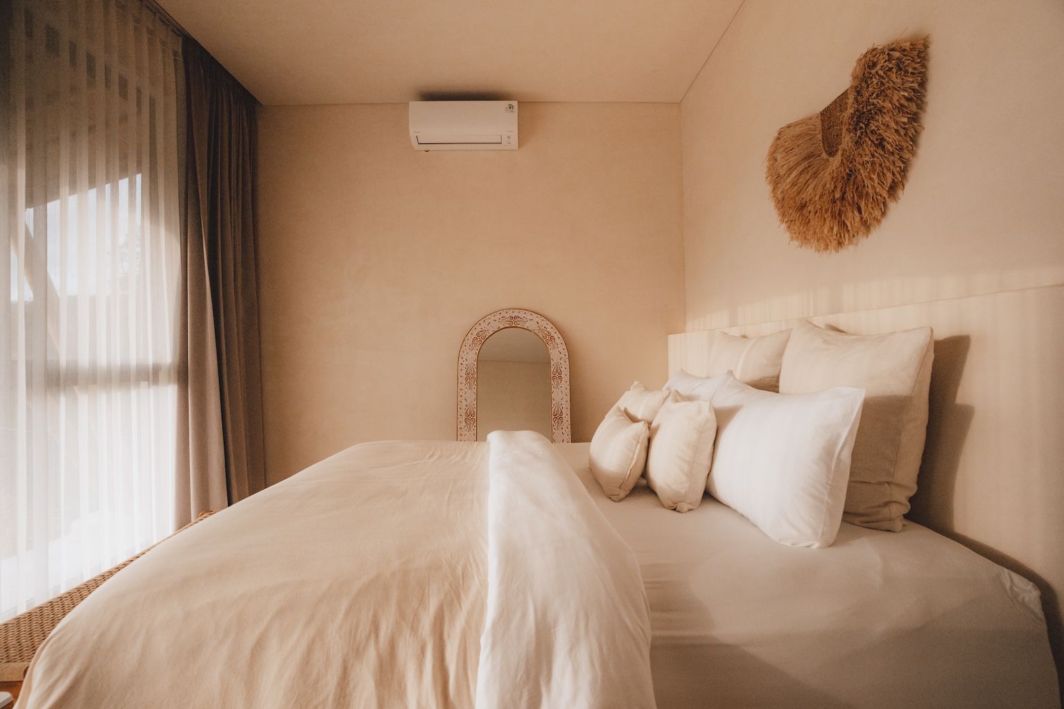Cozy beige bedroom with a neatly made bed, sheer curtains, wall art, and warm natural light