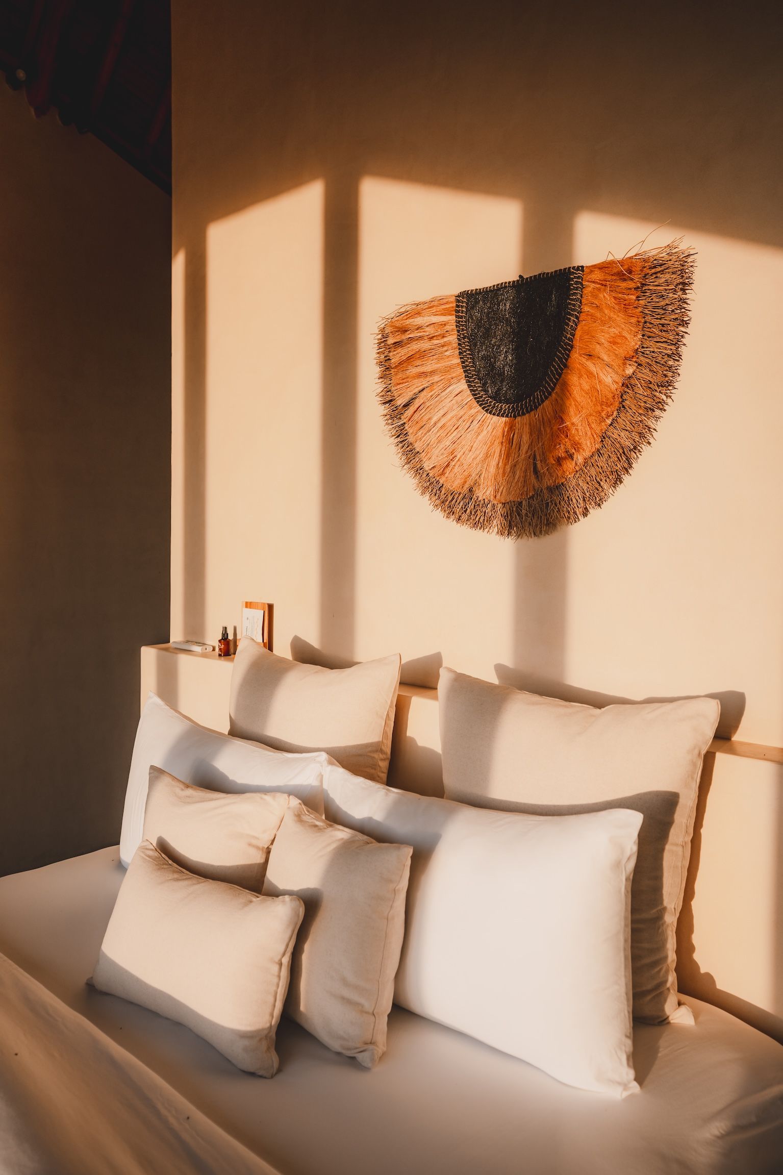 Bed with white pillows beneath a warm sunlit wall hanging in a cozy bedroom