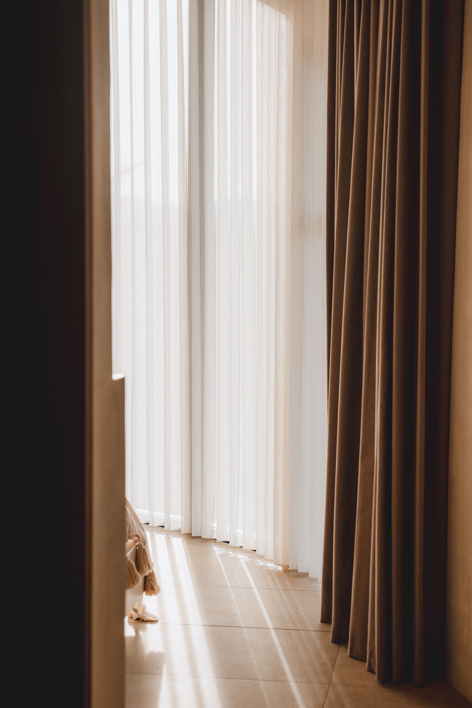 Sunlit room with sheer white curtains and dark drapes, light streaming onto a wooden floor